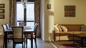 Un comedor con mesa y sillas de madera, una araña y vistas a través de una ventana con cortinas.