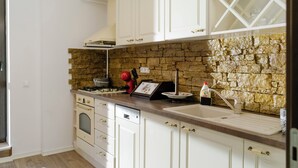 Una cocina con armarios blancos, salpicadero de piedra, estufa a gas y un lavamanos.