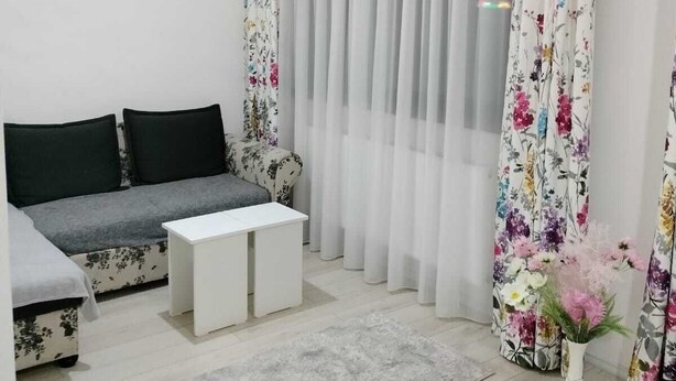 A modern living room with a grey sofa, white coffee table, and floral curtains. - Cozy Flowers Studio • Near Coresi Mall (Brașov)