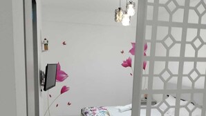 A bedroom with a bed, a bedside table with a plant, a wall-mounted TV, and a decorative wall with pink floral patterns. - Cozy Flowers Studio • Near Coresi Mall (Brașov)