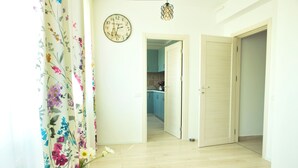 A hallway with a floral curtain, a clock, and a door leading to a kitchen. - Cozy Flowers Studio • Near Coresi Mall (Brașov)
