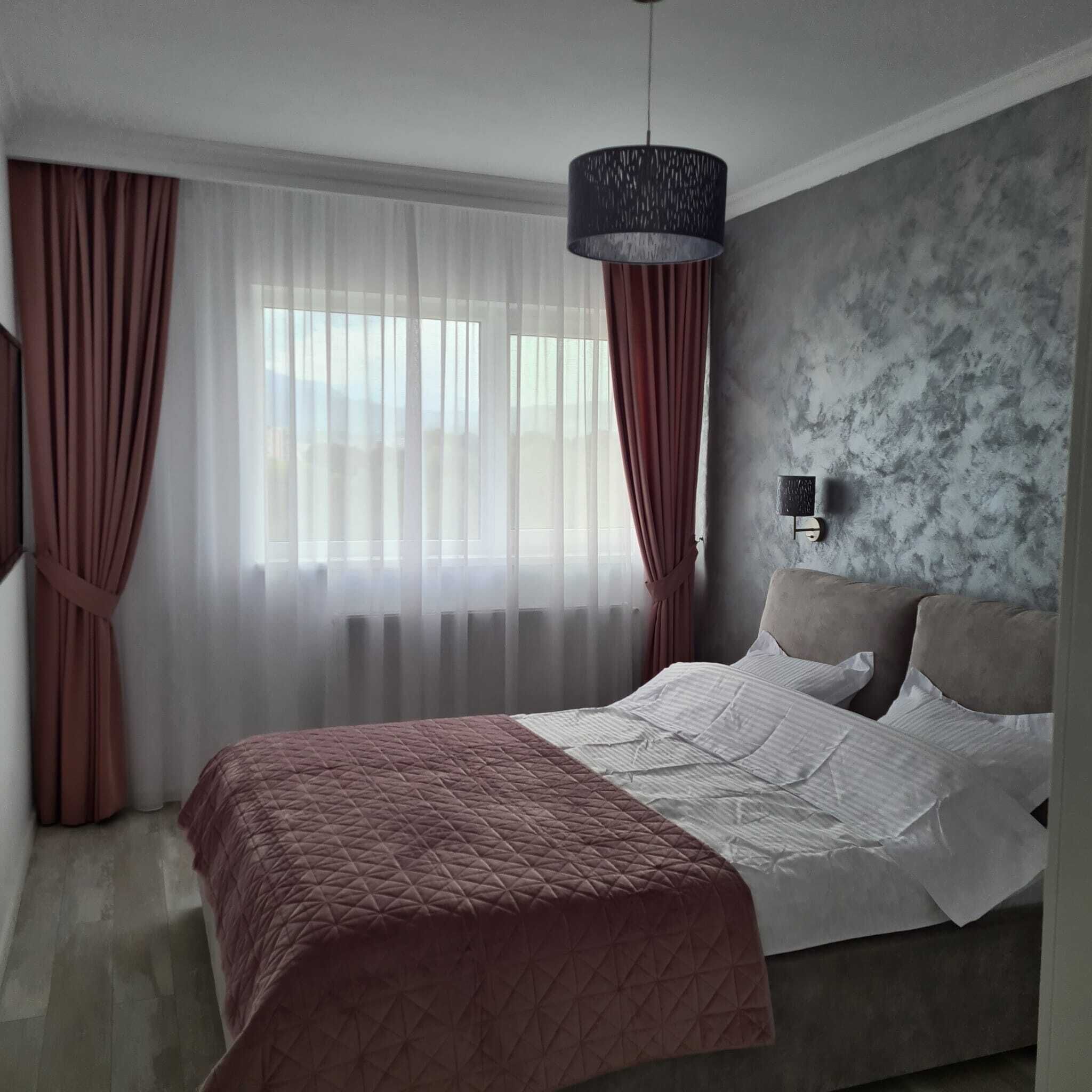 Een moderne slaapkamer met een groot bed, dunne gordijnen, een donkere hanglamp en een structuurwand.