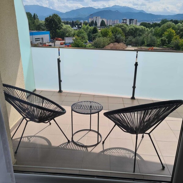 A balcony with three black chairs and a small round table, overlooking a body of water and distant mountains.