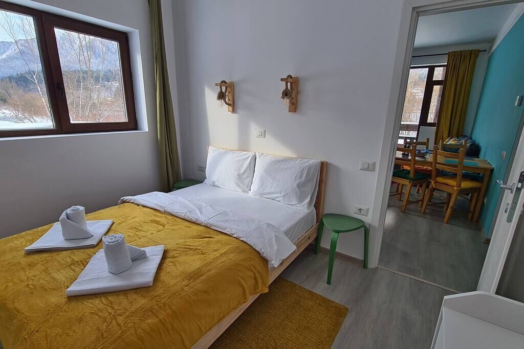A bedroom with a bed, a window, a green chair, and a dining area with chairs and a table.