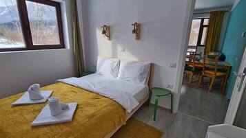 A bedroom with a bed, a window, a green chair, and a dining area with chairs and a table.