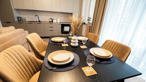 Une table à manger dressée avec des assiettes, des verres et un vase contenant des fleurs séchées, entourée de chaises rembourrées.
