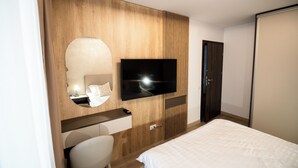 Une chambre d’hôtel moderne avec un mur d’accent en bois, un téléviseur à écran plat, une table de chevet avec une lampe, une chaise blanche et un grand lit.