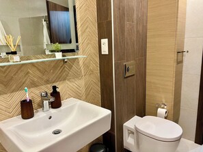 Ein modernes Badezimmer mit einem großen, weißen Waschbecken, einem Spiegel darüber, einer Toilette und einem Duschbereich.