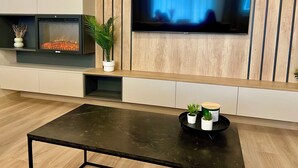 Un salon moderne avec un téléviseur à écran plat fixé à un mur en bois, une table basse noire et une cheminée agrémentée d’objets décoratifs.