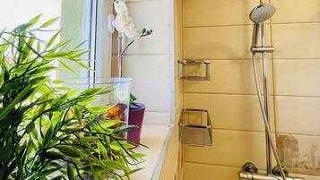 A bathroom with a shower, a window with plants, and a towel rack.