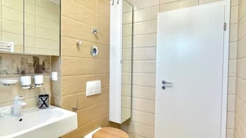 Casa de banho com lavatório, espelho, sanita e porta.