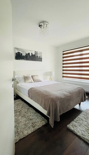 Un dormitorio moderno con una cama, un cuadro de un paisaje urbano, una araña y una ventana con persianas.