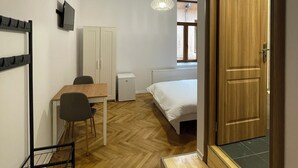 A compact room with a bed, a desk, a chair, a small radiator, and a television on the wall. - Schei Central Studio 3 in the heart of Brasov (Brașov)