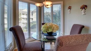 A dining area with a glass table, two chairs, a vase of flowers, and a ceiling light fixture.