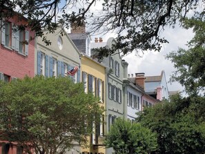 A row of colorful buildings with shutters, a flag, and trees in the foreground.