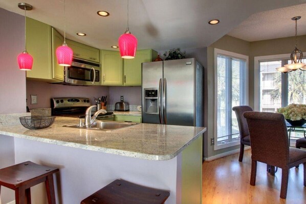 A modern kitchen with green cabinets, stainless steel appliances, and a granite countertop.