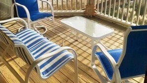 Ein Balkon mit Holzboden, zwei blaue Lounge-Stühle, ein kleiner weißer Tisch und Blick auf den Strand.