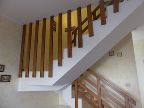 A staircase with wooden handrails and a white wall with a few framed pictures. - Villetta Puccini 121 (Ravenna)