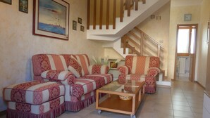 Ein Wohnzimmer mit einer Couch, Sesseln und einem Couchtisch. Eine Treppe führt zu einer oberen Ebene.
