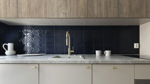 Une cuisine moderne dotée d’un plan de travail en marbre, d’un robinet doré et d’un pare-feu orné d’un motif géométrique.