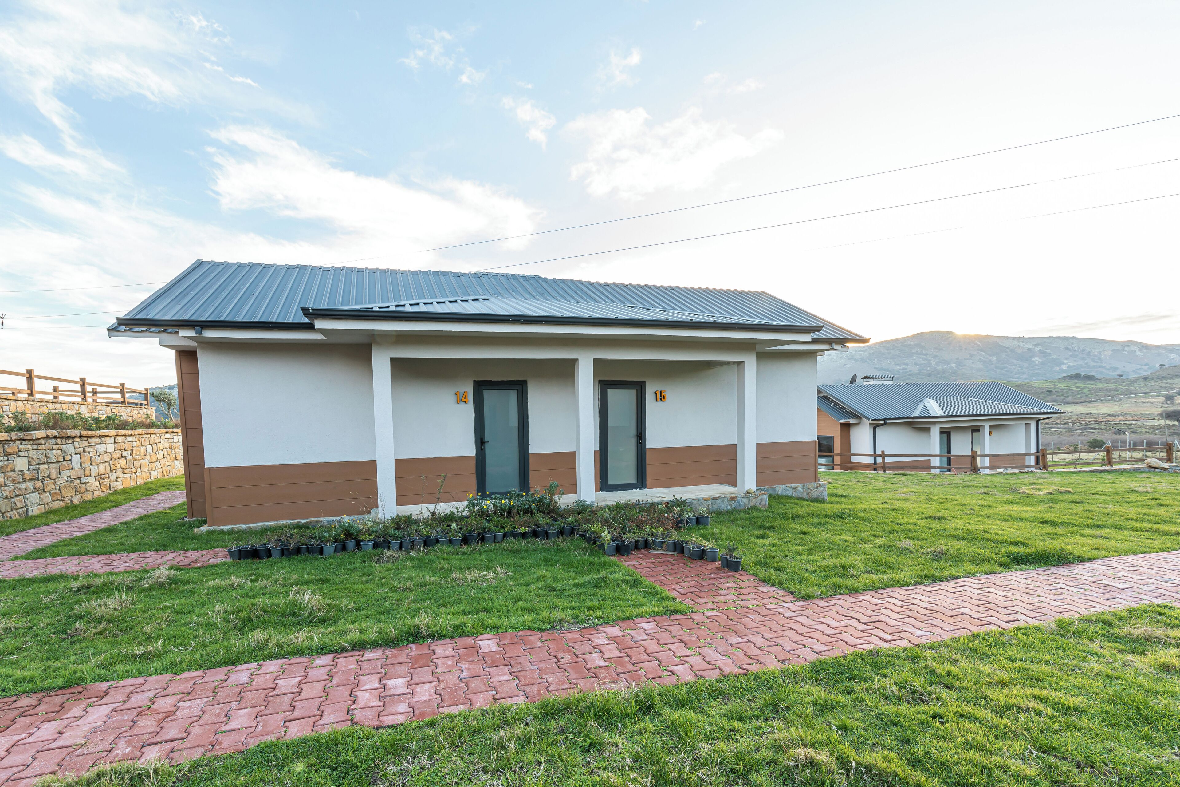 A small, single-story building with a metal roof, a brick pathway leading to the entrance, and a grassy lawn.