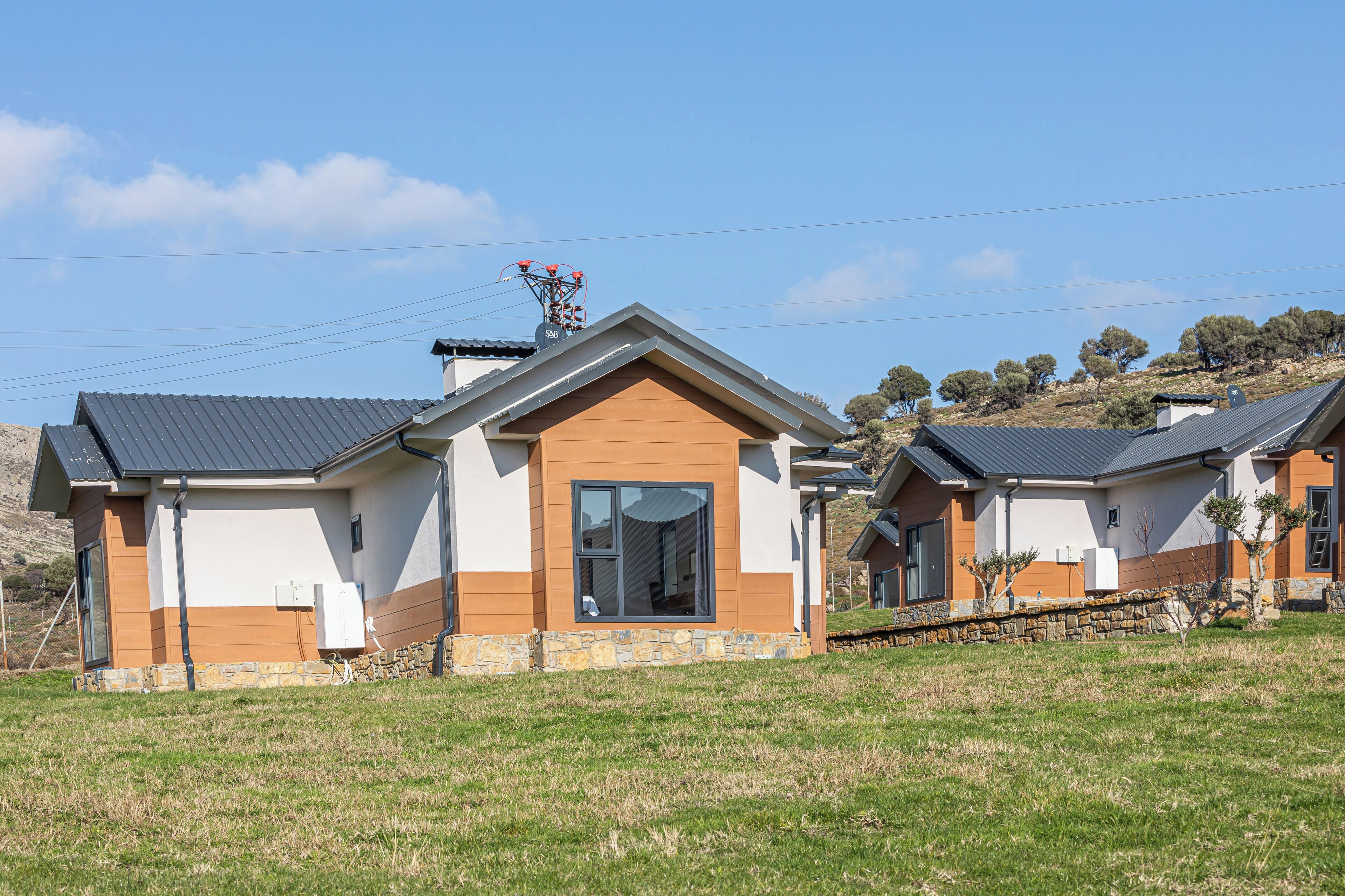 Two modern houses with sloped roofs, a stone foundation, and a clear blue sky in the background.