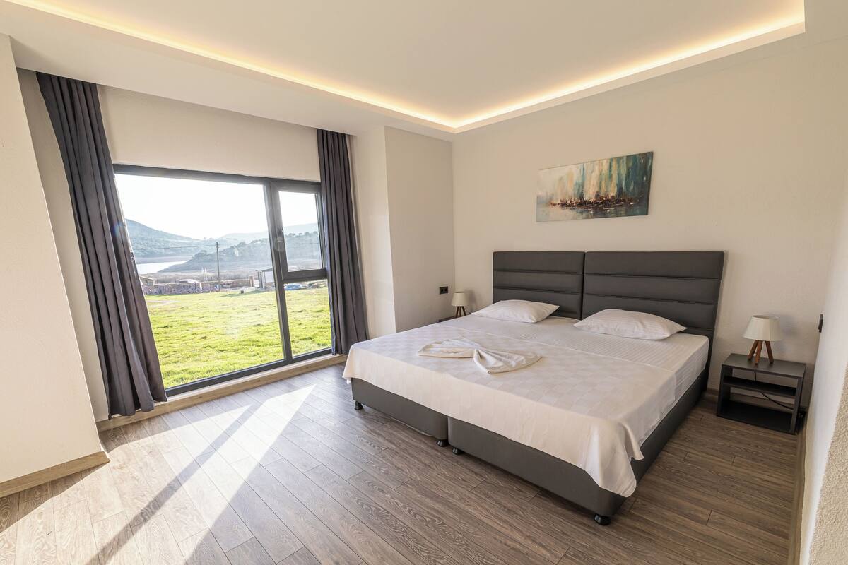 A modern hotel room with a large bed, a view of the outdoors, and a painting on the wall.