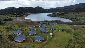 A residential area with houses arranged in a semi-circular pattern around a central road, with a lake and hills in the background. - Tolstoy’un Bisikleti Gökçeada (Gökçeada)