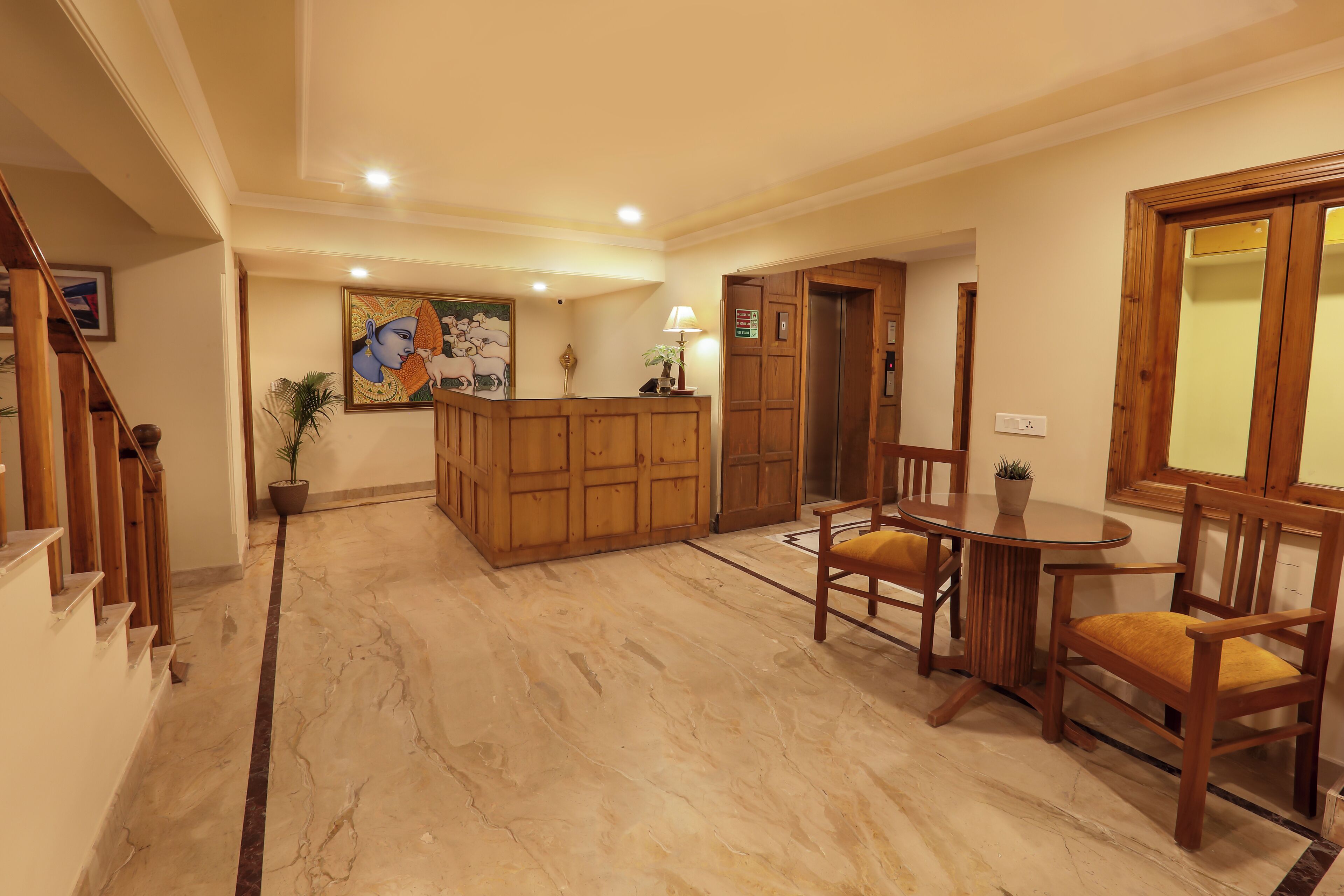 A reception area with a wooden desk, chairs, a potted plant, and a painting on the wall.