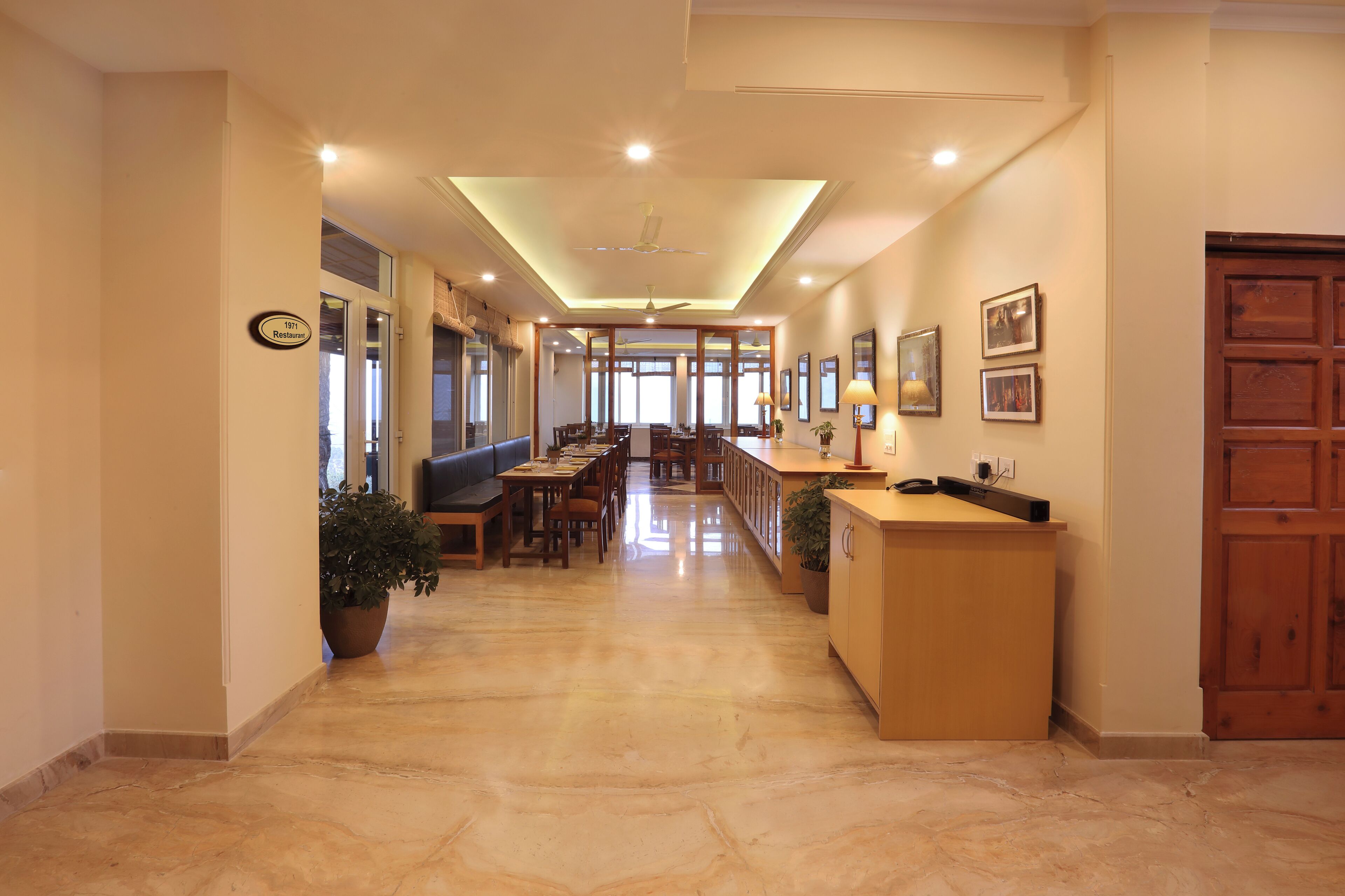 Un pasillo de hotel con una recepción, zona de estar y vistas al comedor.