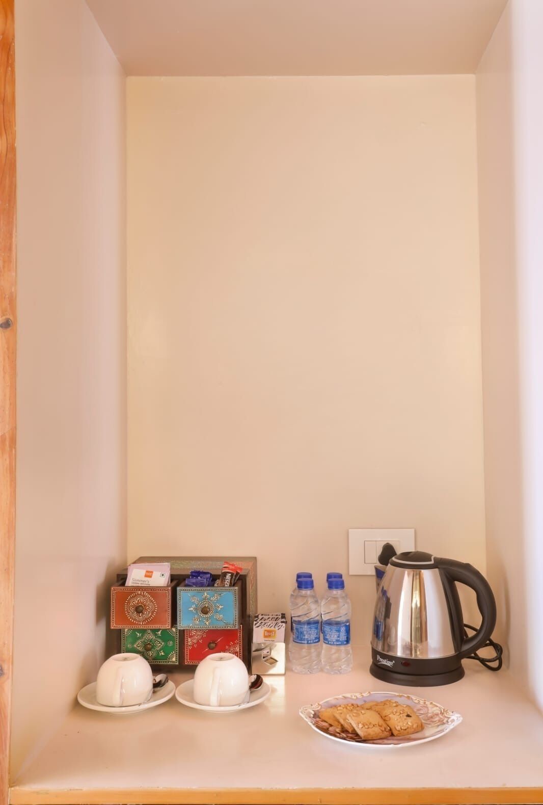 Une petite cuisine équipée d’une machine à café, de deux bouteilles d’eau, d’une assiette de biscuits et d’une boîte de thé.