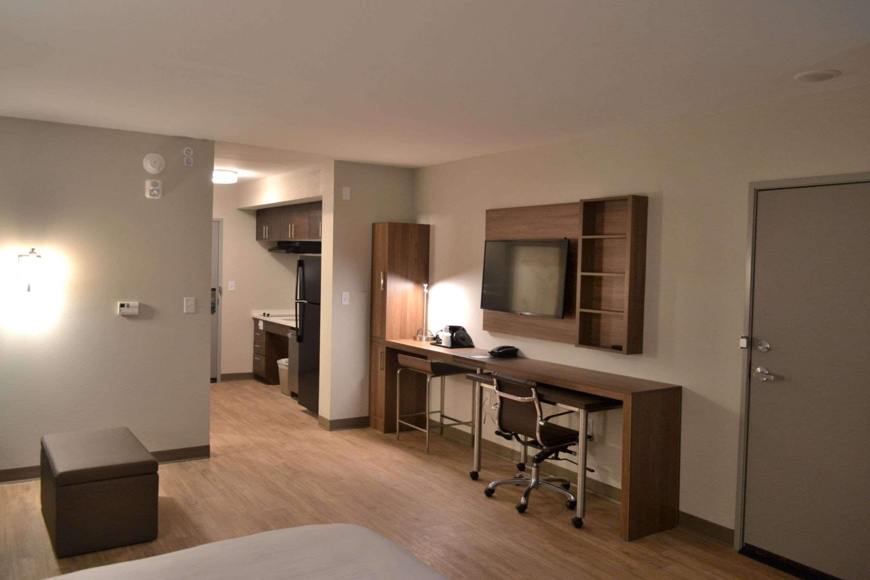 A hotel room with a bed, a desk with a chair, a TV mounted on the wall, and a wardrobe.