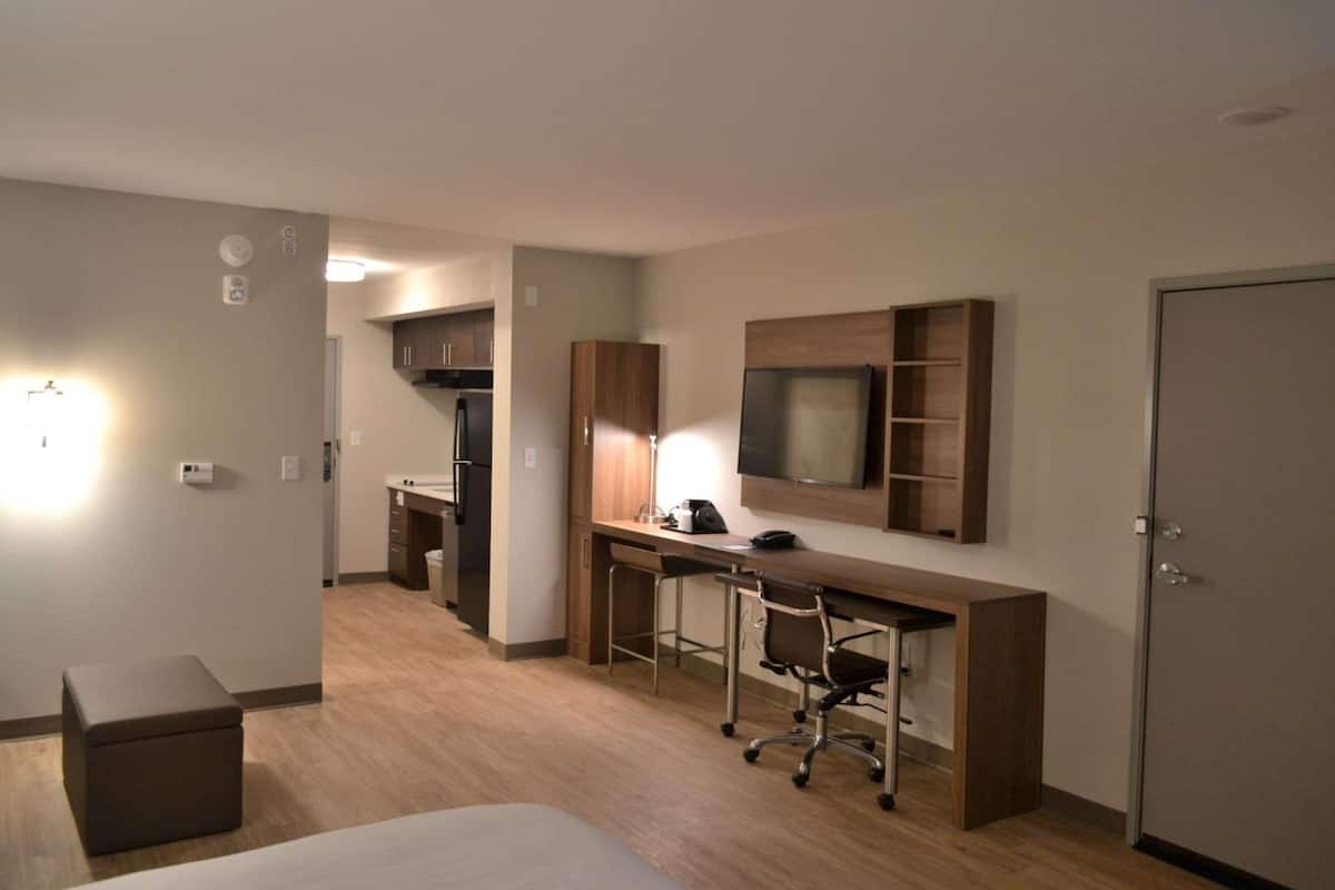 A hotel room with a bed, a desk with a chair, a TV mounted on the wall, and a wardrobe.