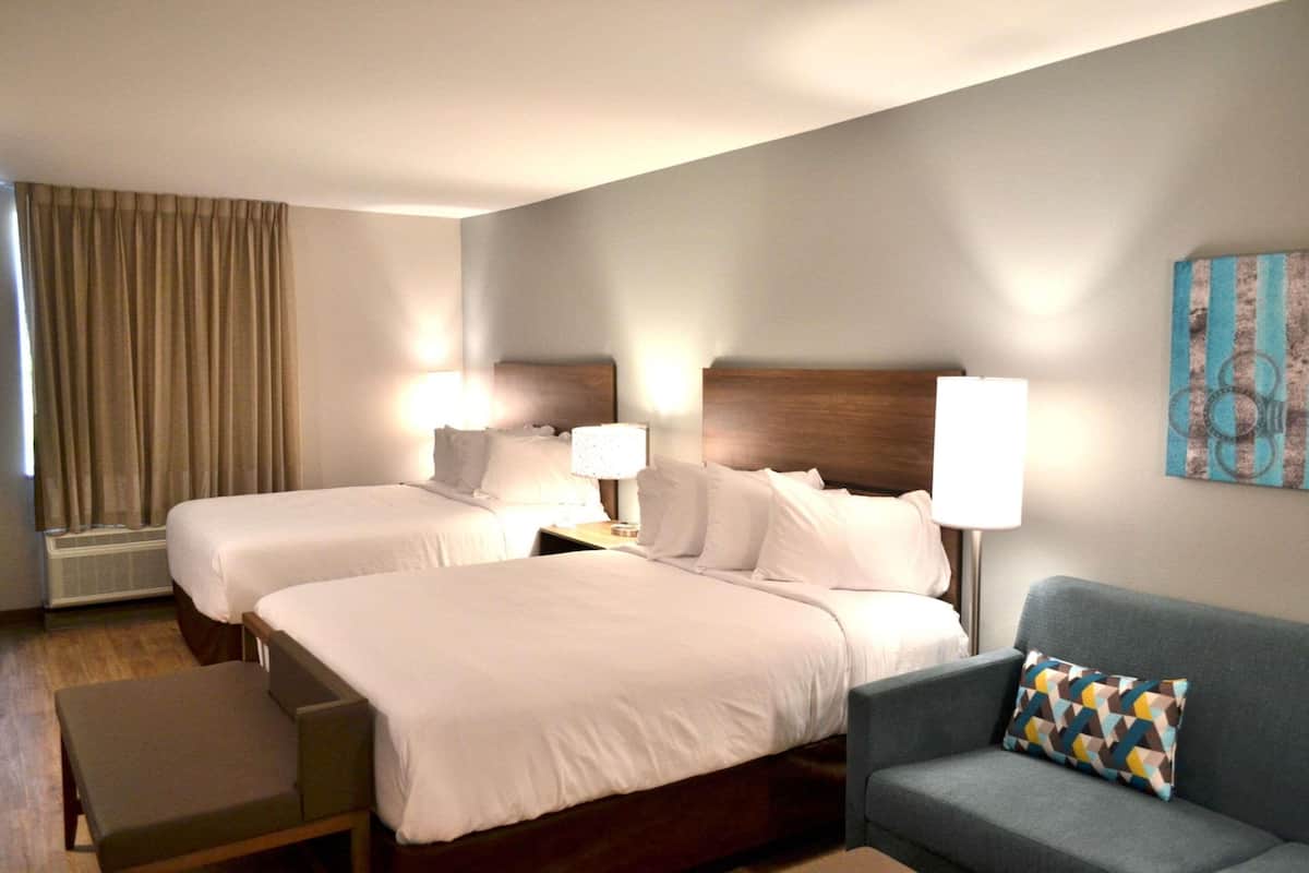 A hotel room with two beds, a sofa, and a wall-mounted artwork.