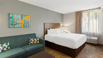 A hotel room with a bed, a sofa, a coffee table, and a painting on the wall.