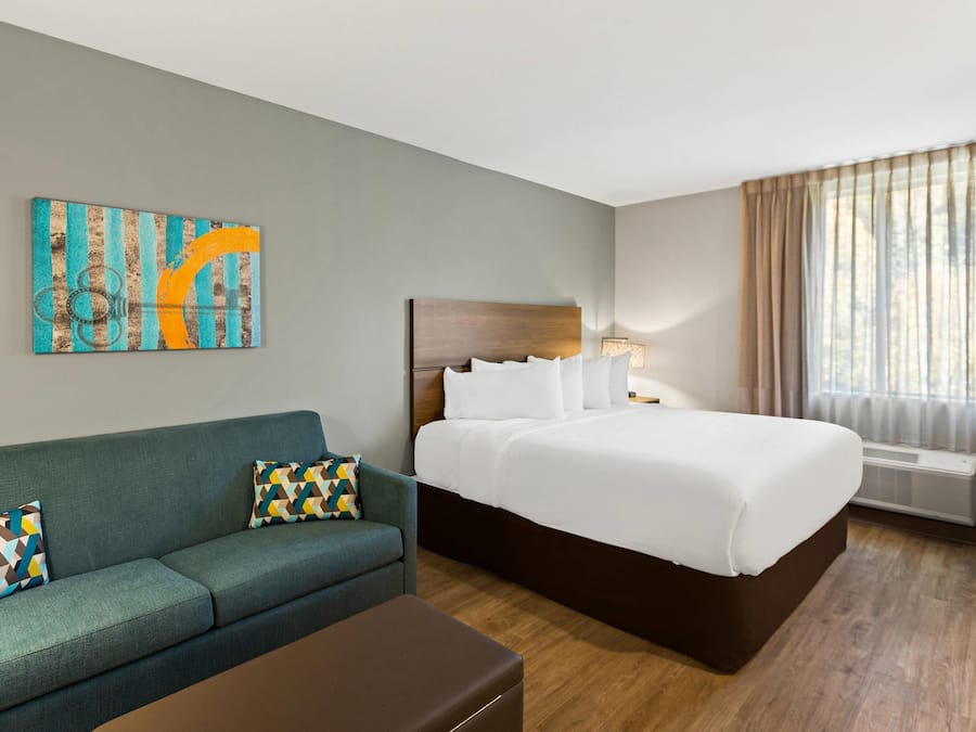Una habitación de hotel con cama, sofá, mesa de centro y un cuadro en la pared.