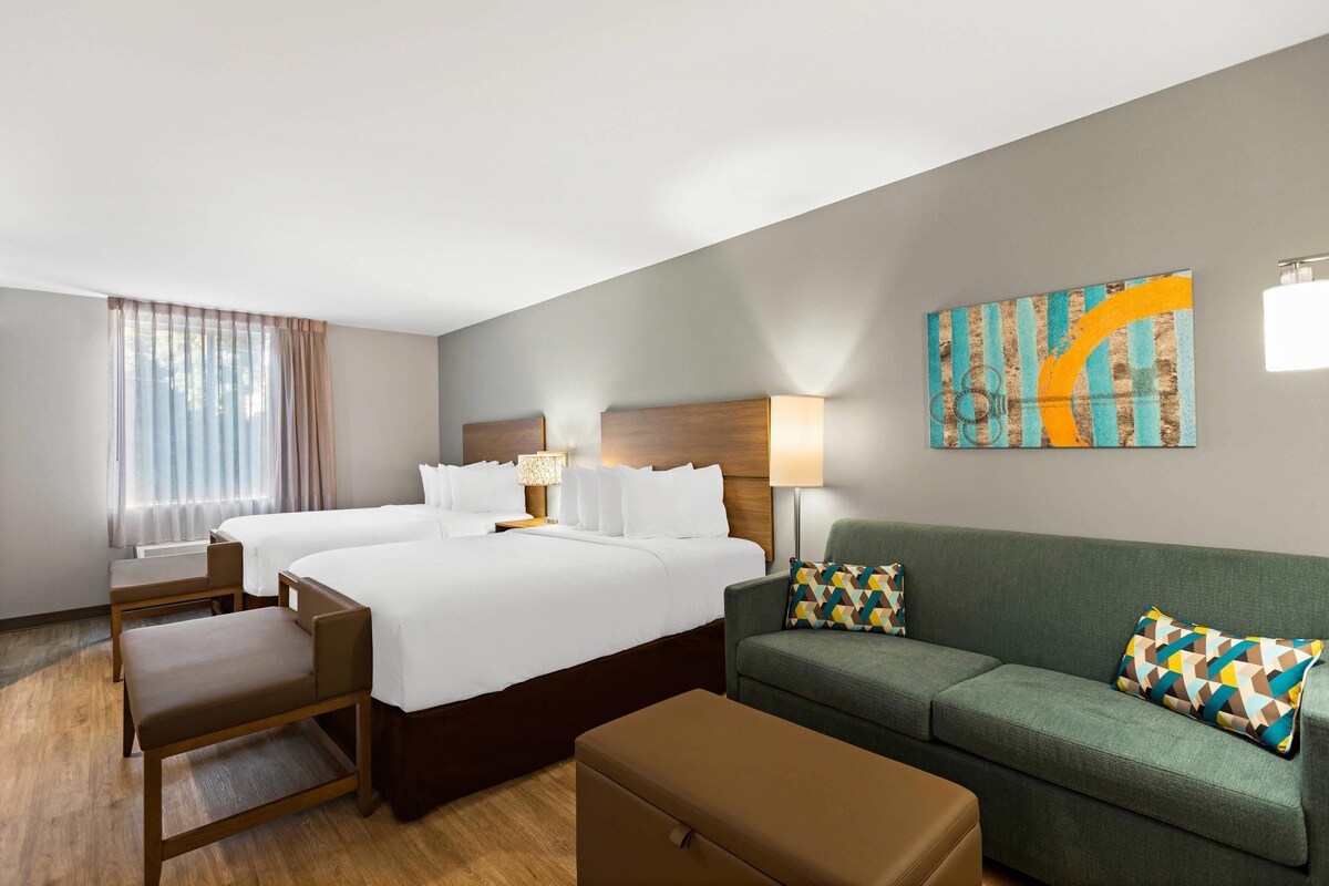 A hotel room with two beds, a sofa, a chair, a table, and a painting on the wall.