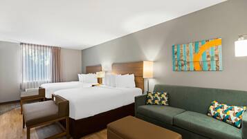 A hotel room with two beds, a sofa, a chair, a table, and a painting on the wall.