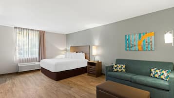 Een hotelkamer met een groot bed, een bank, een salontafel, een nachtkastje met een lamp en een schilderij aan de muur.