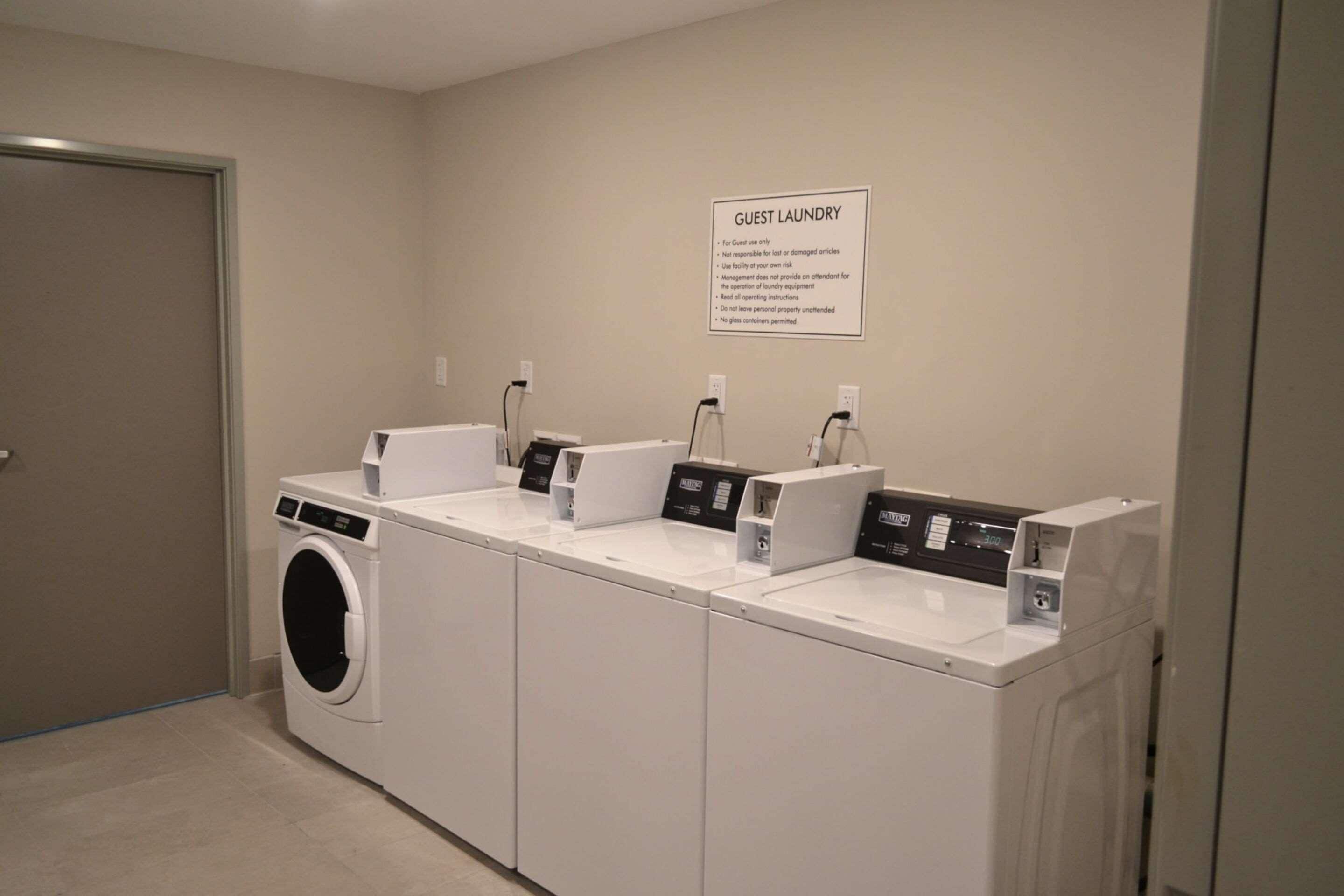 A guest laundry area with multiple washing machines and dryers, a sign with usage instructions, and a door to the left.