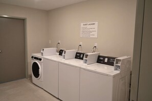 A guest laundry area with multiple washing machines and dryers, a sign with usage instructions, and a door to the left. - Mainstay Suites Gatlinburg TN (Gatlinburg)