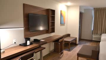 Habitación de hotel con escritorio de madera, televisor de pantalla plana, máquina de café y una silla.