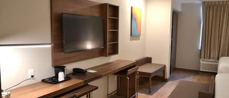 Een hotelkamer met een houten bureau, een flatscreen televisie, een koffiezetapparaat en een stoel.