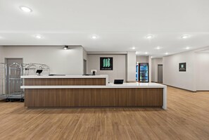 A modern reception area with a wooden reception desk, a metal desk lamp, and a digital screen displaying the hotel's logo. - Mainstay Suites Gatlinburg TN (Gatlinburg)