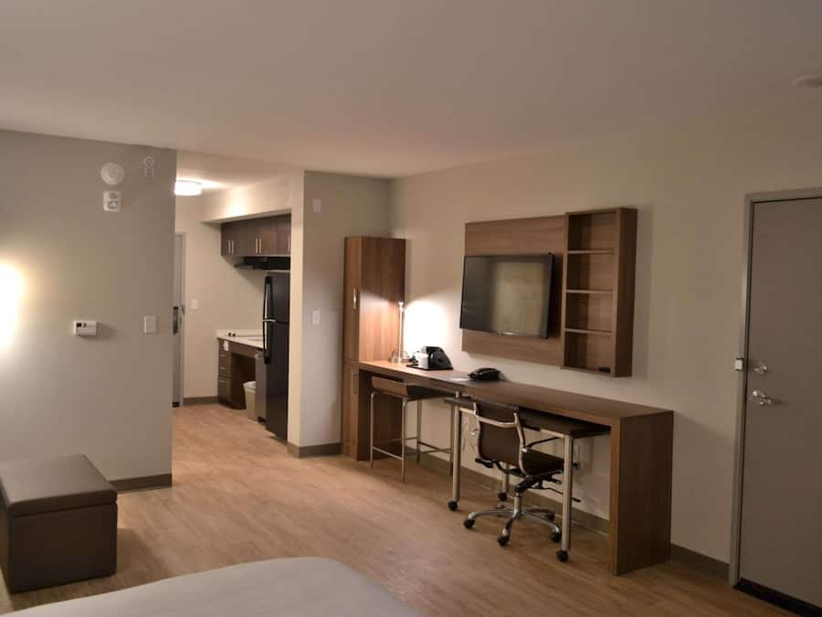 A hotel room with a bed, a desk with a chair, a TV mounted on the wall, and a wardrobe.