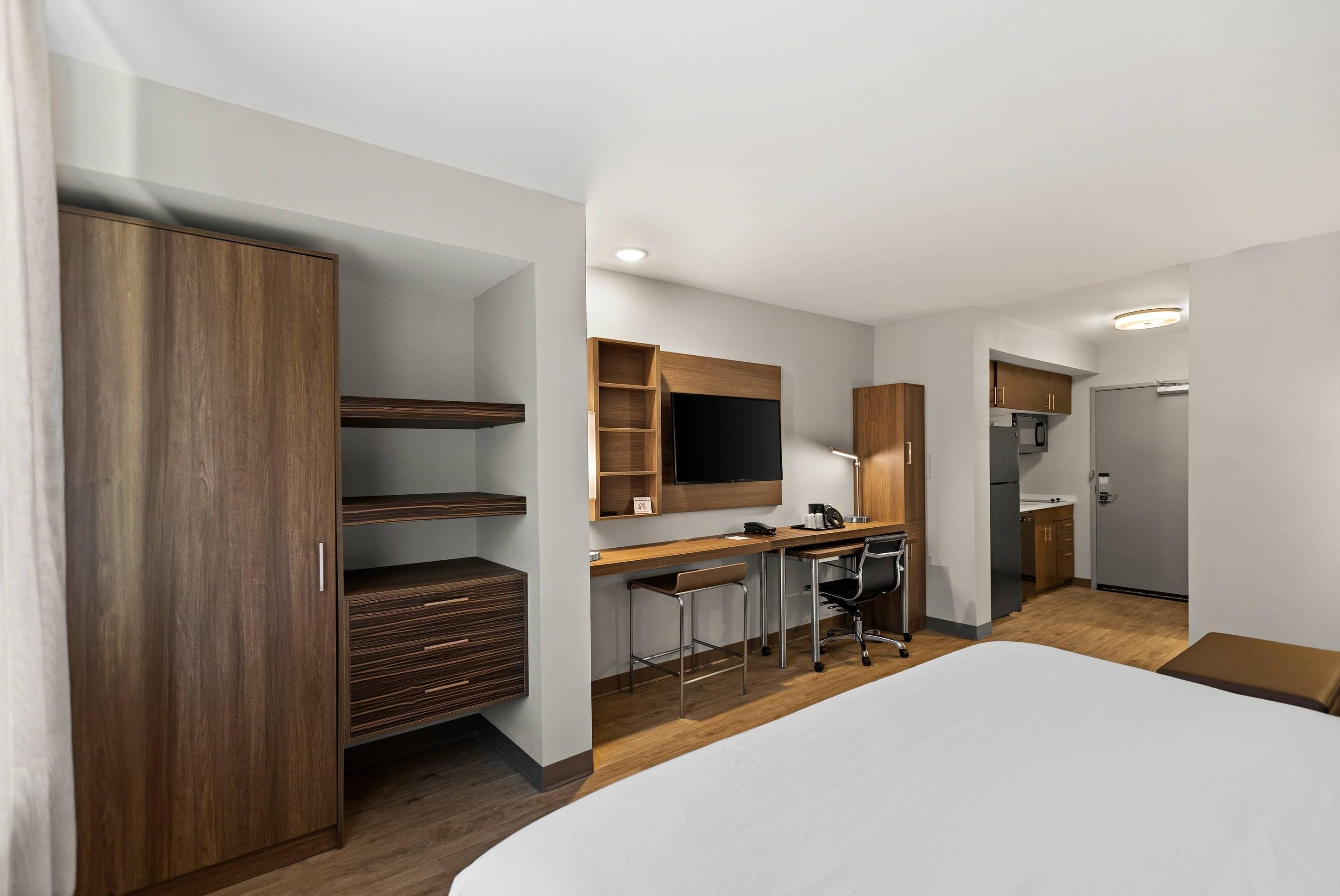 A modern hotel room with a large bed, a desk with a chair, a TV, and a wardrobe.