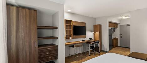 A modern hotel room with a large bed, a desk with a chair, a TV, and a wardrobe.