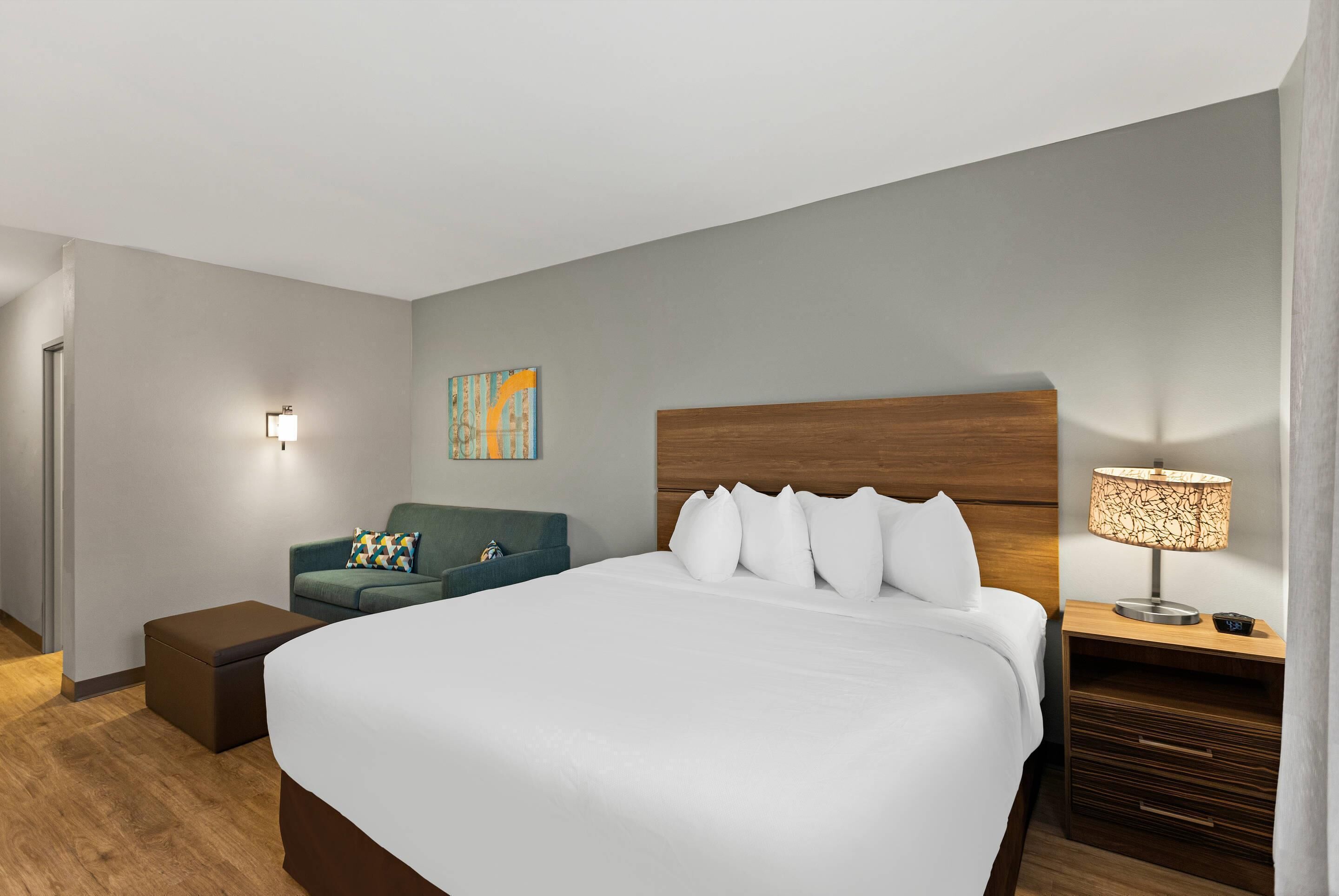 A hotel room with a large bed, a nightstand with a lamp, a chair, and a small table.