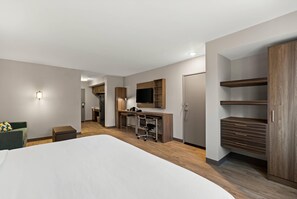 A hotel room with a large bed, a desk with a chair, a television, and built-in wardrobes.