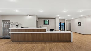 A modern reception area with a wooden reception desk, a metal desk lamp, and a digital screen displaying the hotel's logo.